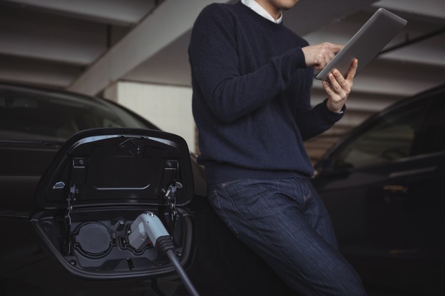 man using digital tablet while electric car